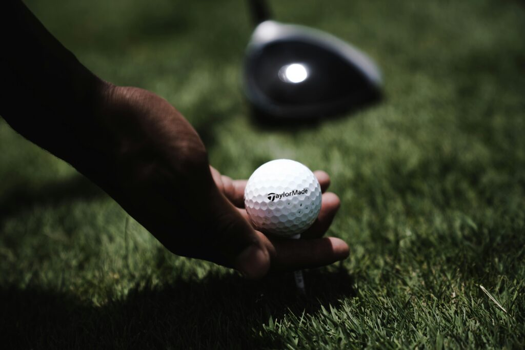 Close-up image of a hand holding a golf ball on a grassy field, emphasizing the sport of golfing.