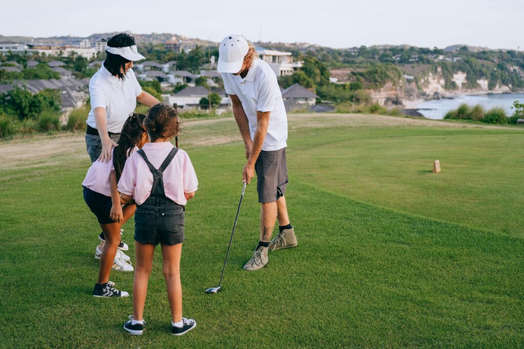 A family enjoying a golf lesson together on a sunny day at a beautiful coastal golf course.